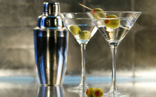 Two glasses of classic martini garnished with olives and a cocktail shaker.
