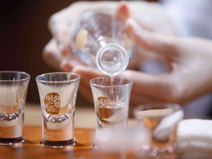 Baijiu is being poured into short glasses through a bottle. 